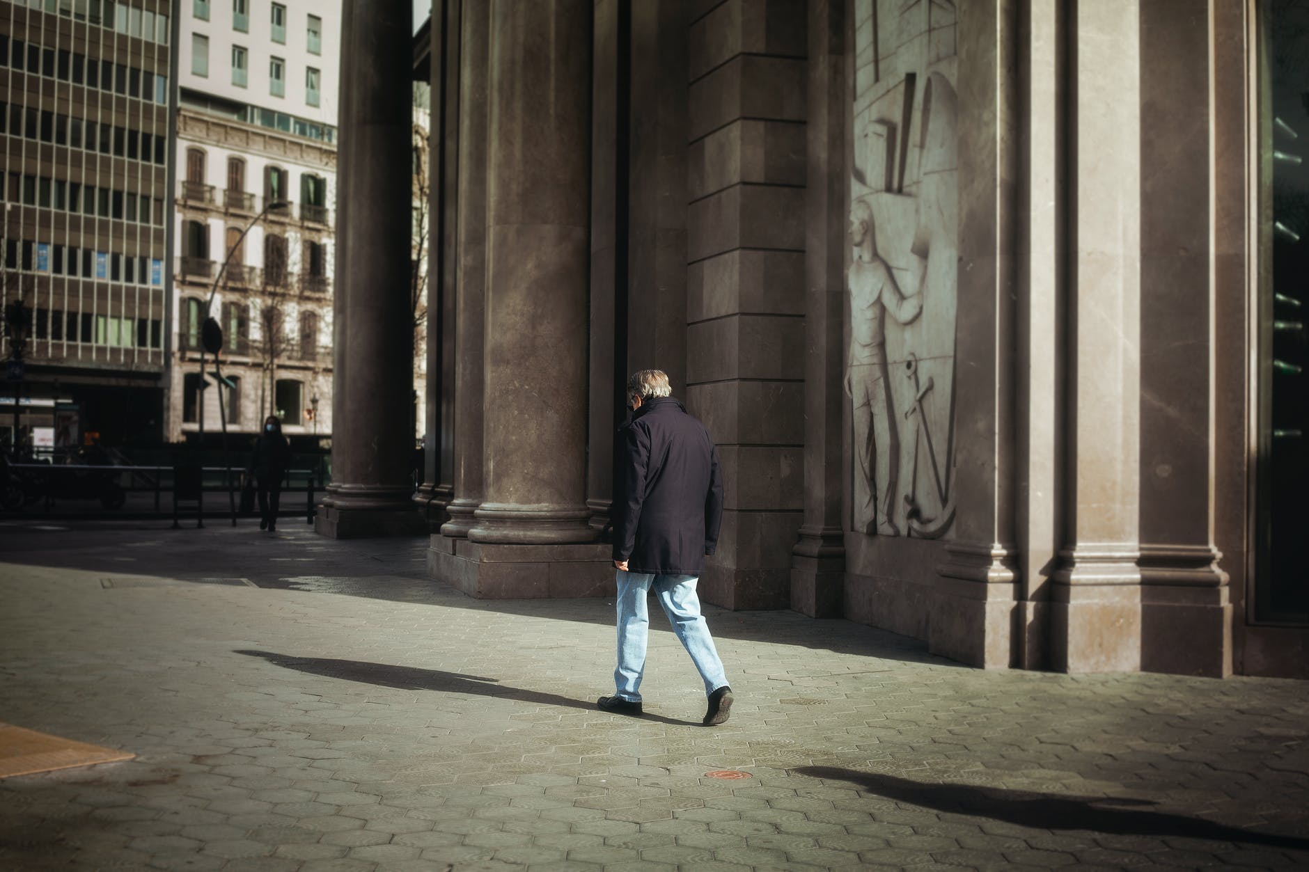 man in black jacket and blue denim jeans walking on sidewalk